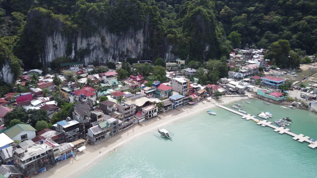 vista aérea: muelle y frente a la playa del puerto de la ciudad de el nido delante de un exuberante fondo tropical de imponentes rocas de piedra caliza, bahía de bacuit - filipinas