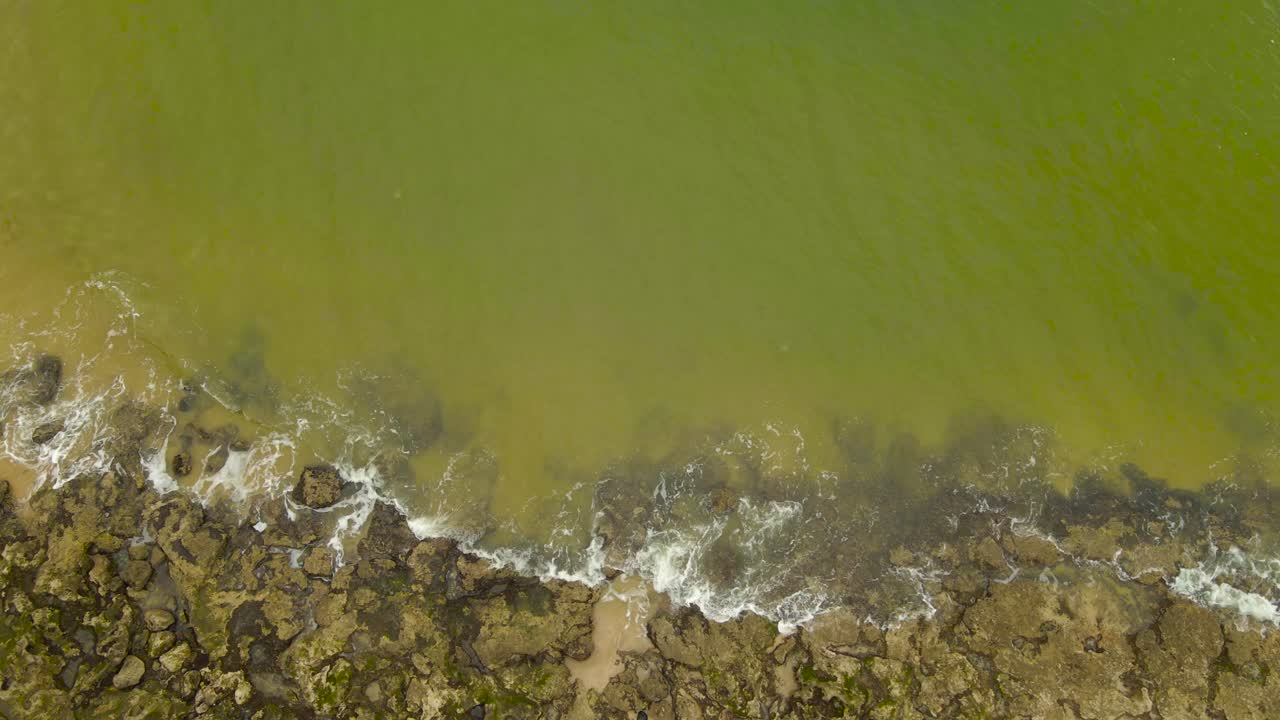 Vista aerea dall'alto di una costa carsica e rocciosa a Paco de Arcos, in Portogallo, con onde verdi e turchesi che si infrangono sulle pietre durante il giorno