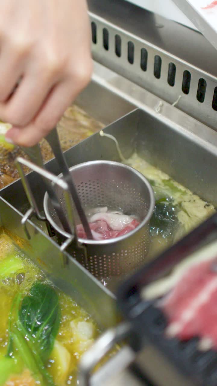 沸騰したレストランの鍋料理で、トングを使って生豚肉を調理する手のクローズアップ。