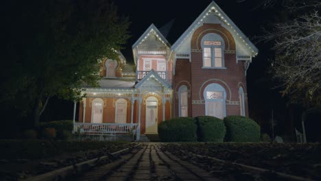 someone is walking up to an old lit up victorian house