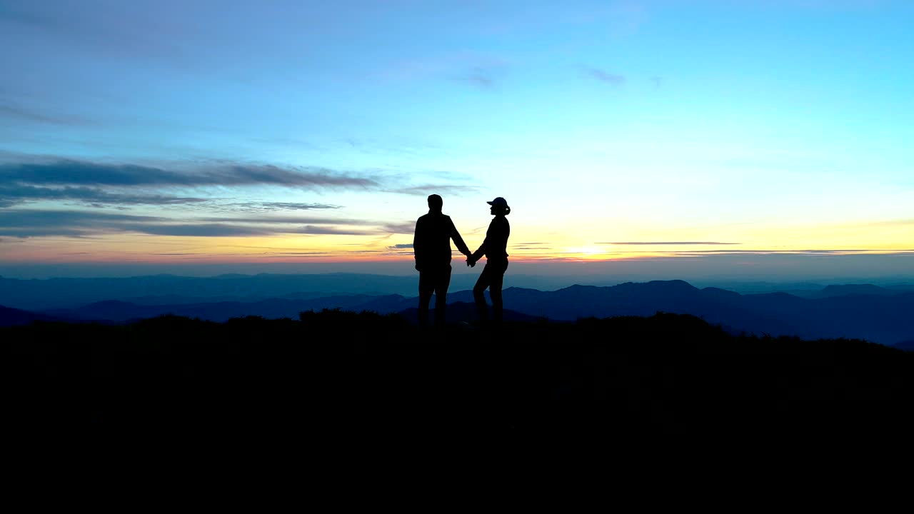 해가 지는 배경에서 산 위에 서 있는 여자와 남자