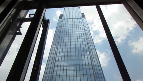 a stunning view of a skyscraper through open windows, showcasing modern architecture against a bright sky with fluffy clouds in a vibrant urban landscape