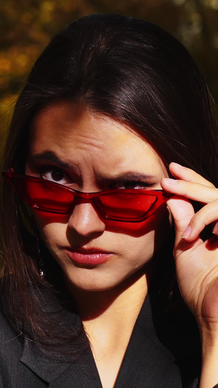 A Young Woman in Stylish Red Sunglasses Poses Confidently Against a Nature-Inspired Background, Capturing Glamour and Attitude with a Striking Look