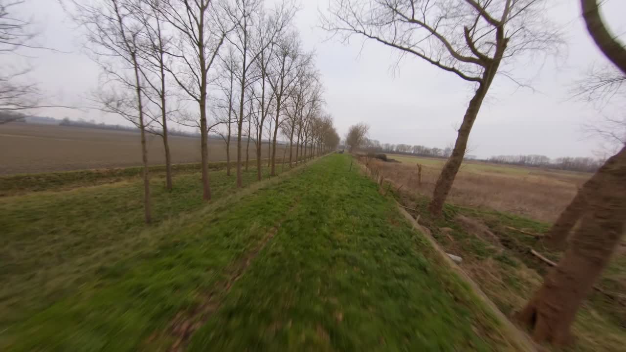 Fast moving above a green dyke surrounded by trees during winter