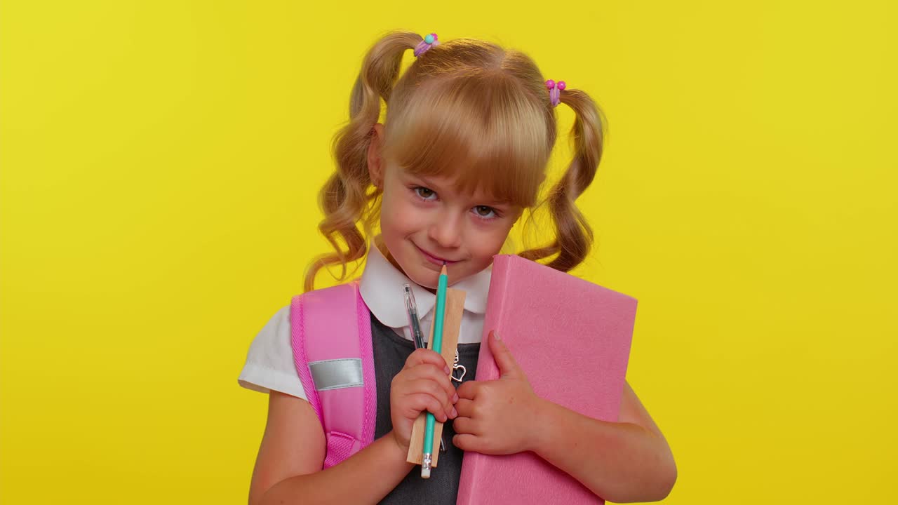 Lustiges, positives Grundschulmädchen mit Pferdeschwänzen in Uniform lächelt auf gelbem Hintergrund.