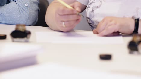 female hand writting oldschool black ink pen on the white sheet of paper close  up slow motion in focus ine  class room