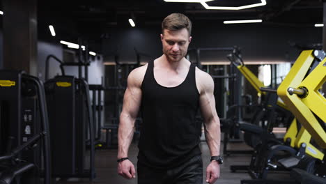 portrait of a fitness man. muscular bodybuilder walking along modern gym after his workout. handsome athletic man in black singlet in sports centre.