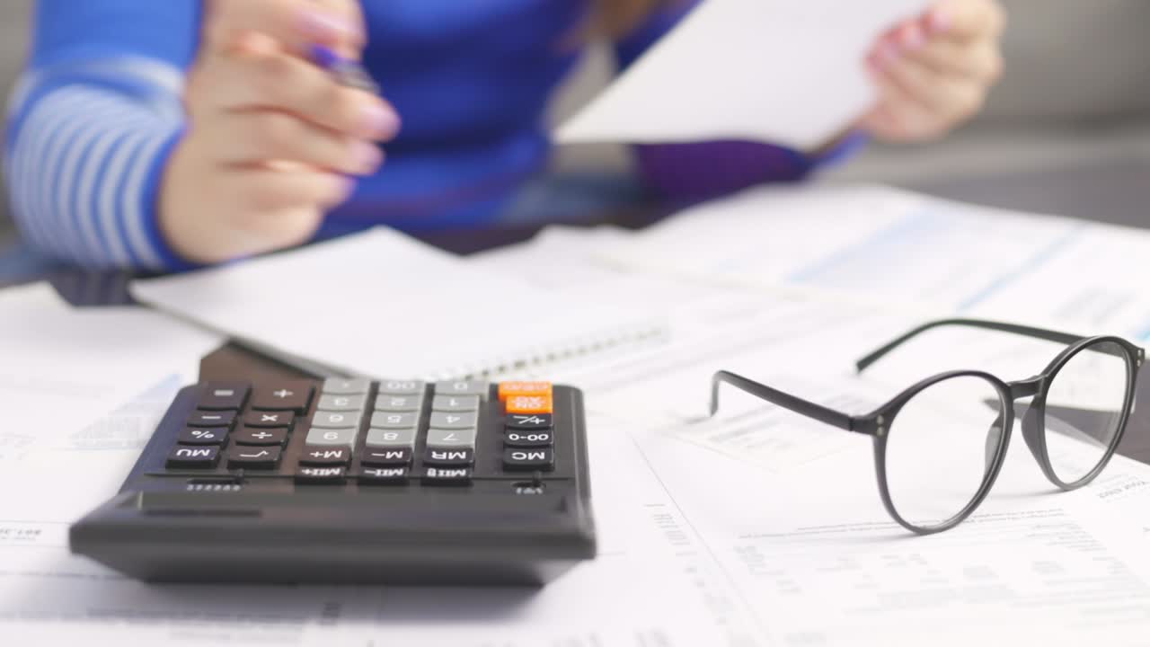 mujer usando calculadora para calcular facturas domésticas en el hogar, haciendo papeleo para pagar impuestos
