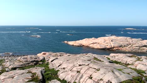 boats cruising across the blue sea viewed from rocky coast of bohuslan with granite in gotaland, sweden