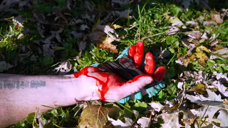 Topdown-view-Man-with-tattooed-arm-falls-in-green-grass-among-fallen-autumn-leaves,-Bloody-hand-with-spasms-Concept