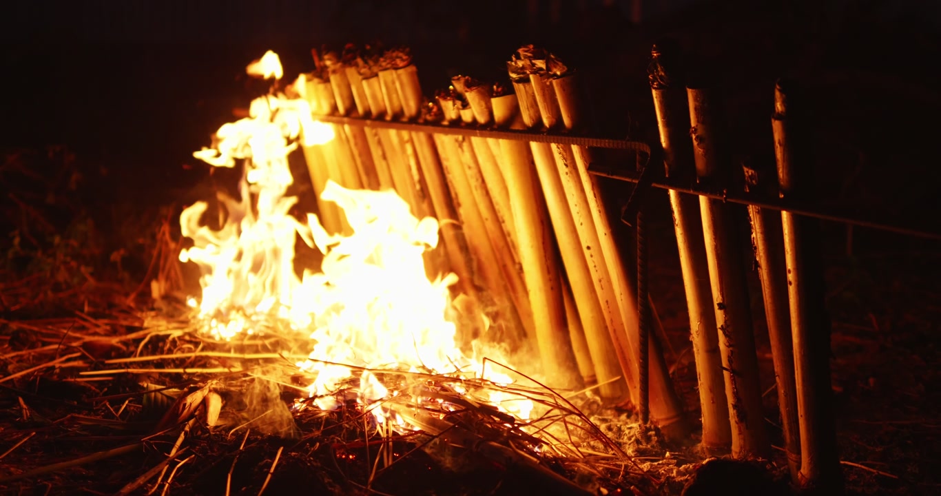 Traditional bamboo sticky rice cooking over an open fire, representing local food preparation and outdoor rural lifestyle.