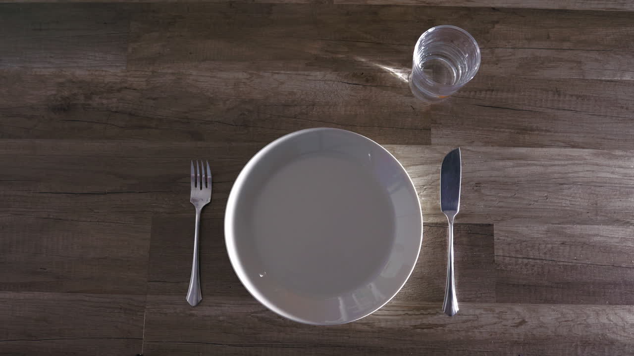 인식할 수 없는 사람이 접시와 식기가 있는 나무 테이블을 설정합니다.