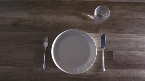 Unrecognizable-person-sets-wooden-table-with-plate-and-cutlery