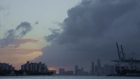 a dramatic wall of clouds approaches the miami skyline during sunset, with cranes silhouetted against the fading light.