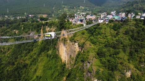 ascending tilt down shot showing suspension bridge and bungee jumping spot in green landscape of nepal - pokhara city in background