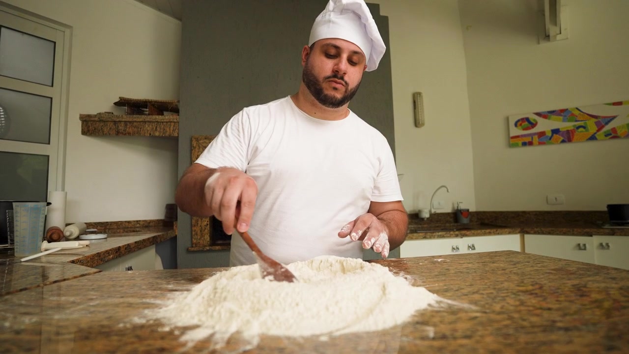 Um chef profissional mistura farinha seca à mão, iniciando o processo de preparo da massa de pizza.