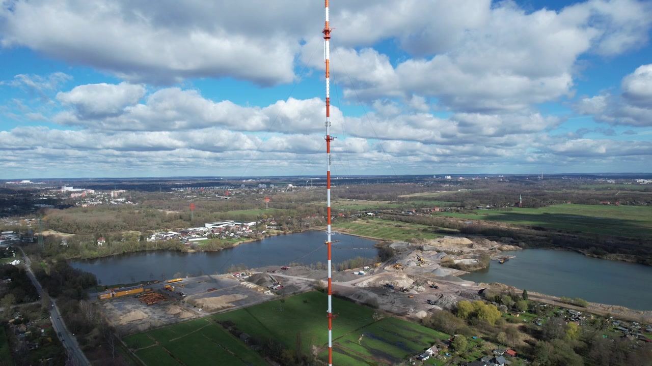 Luchtopname met drone van een rood-witte telecommunicatietoren die uitrijst boven waterwegen, open velden en industriële buitenwijken in Moorfleet, Hamburg, Duitsland