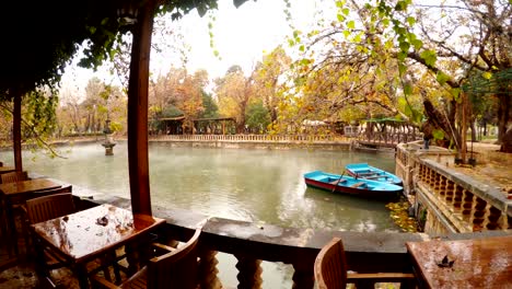 panorama empty restaurant two blue boats moor fog floats under lake ayn-zelih around green and yellow trees park urfa