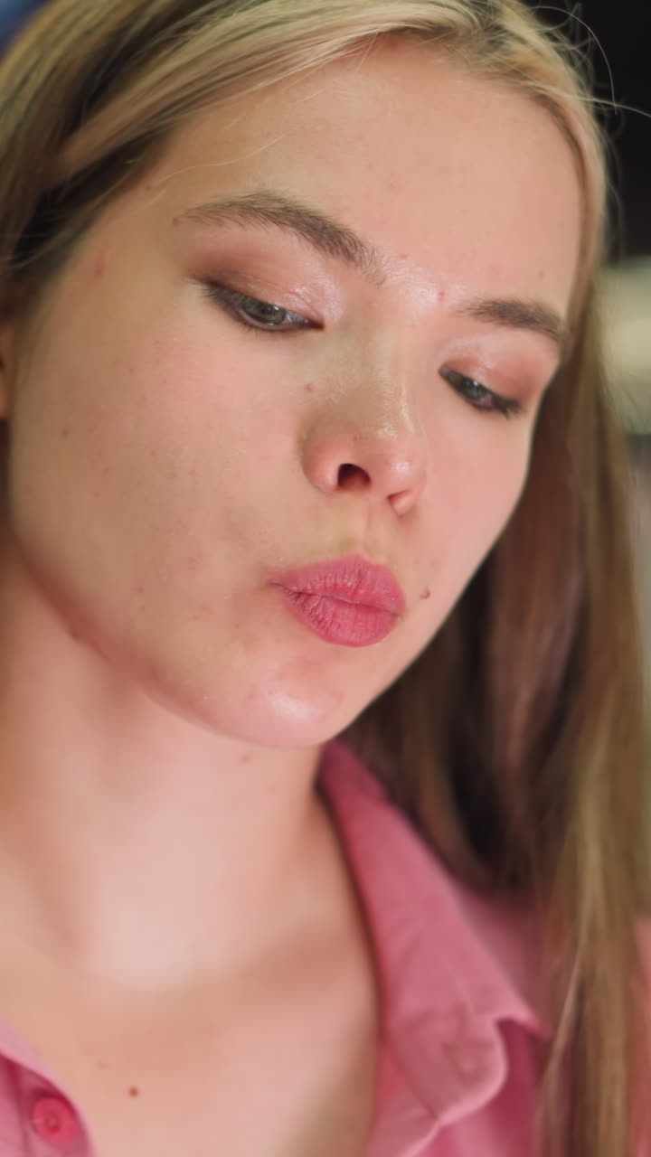 mujer joven sentada en un centro comercial, vestida de rosa, come una patata frita y luego toma una bebida, el fondo presenta un borrón suave de luces brillantes de diversos colores con vista borrosa de la gente