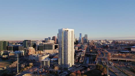 Vista-Aérea-De-Drones-Del-Moderno-Edificio-De-Apartamentos-De-Confluencia-Y-El-Horizonte-De-La-Ciudad-De-Denver-Durante-La-Puesta-De-Sol-De-La-Hora-Dorada