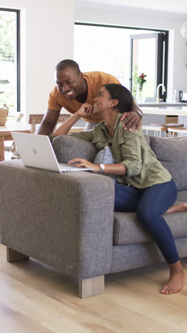 Vertical video: Couple relaxing at home, woman using laptop while man smiling and leaning on couch
