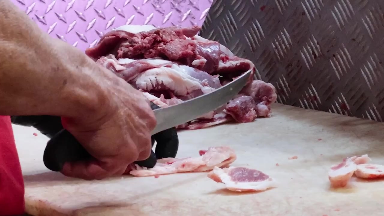 A close-up view of a butcher's hands slicing raw red meat on a white surface.