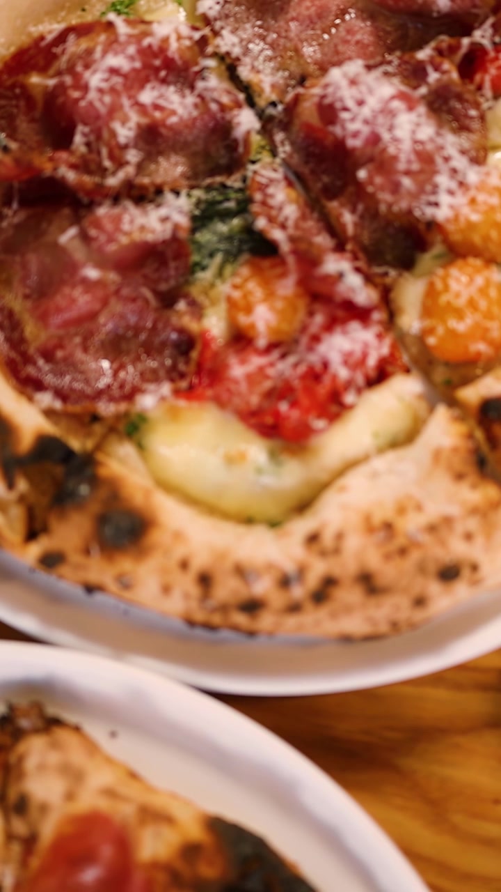 Inquadratura ravvicinata dall'alto di una pizza artigianale cotta nel forno a legna su un tavolo di legno di un ristorante.