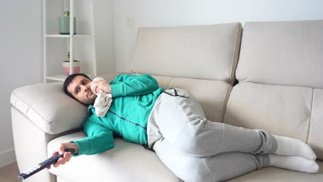 Male with toothache lying on sofa zapping on tv and applying ice