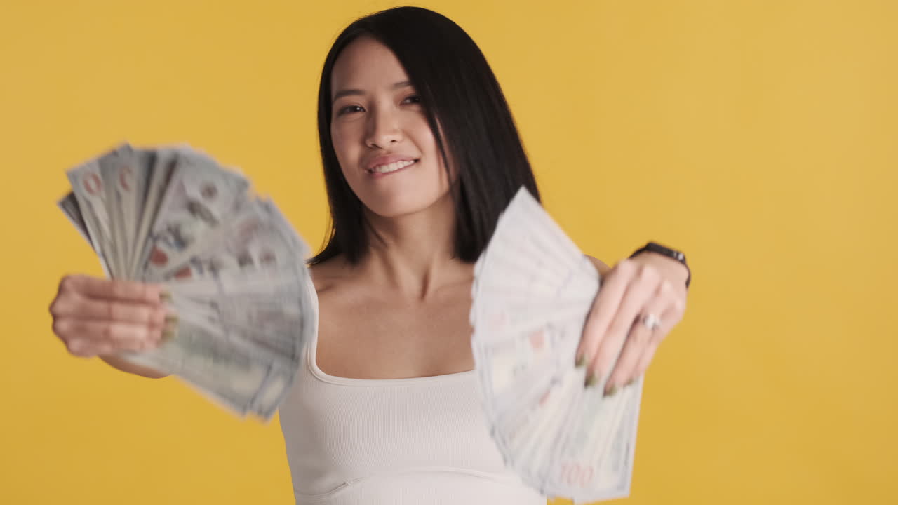 Asian woman looking happy while holding money on camera.
