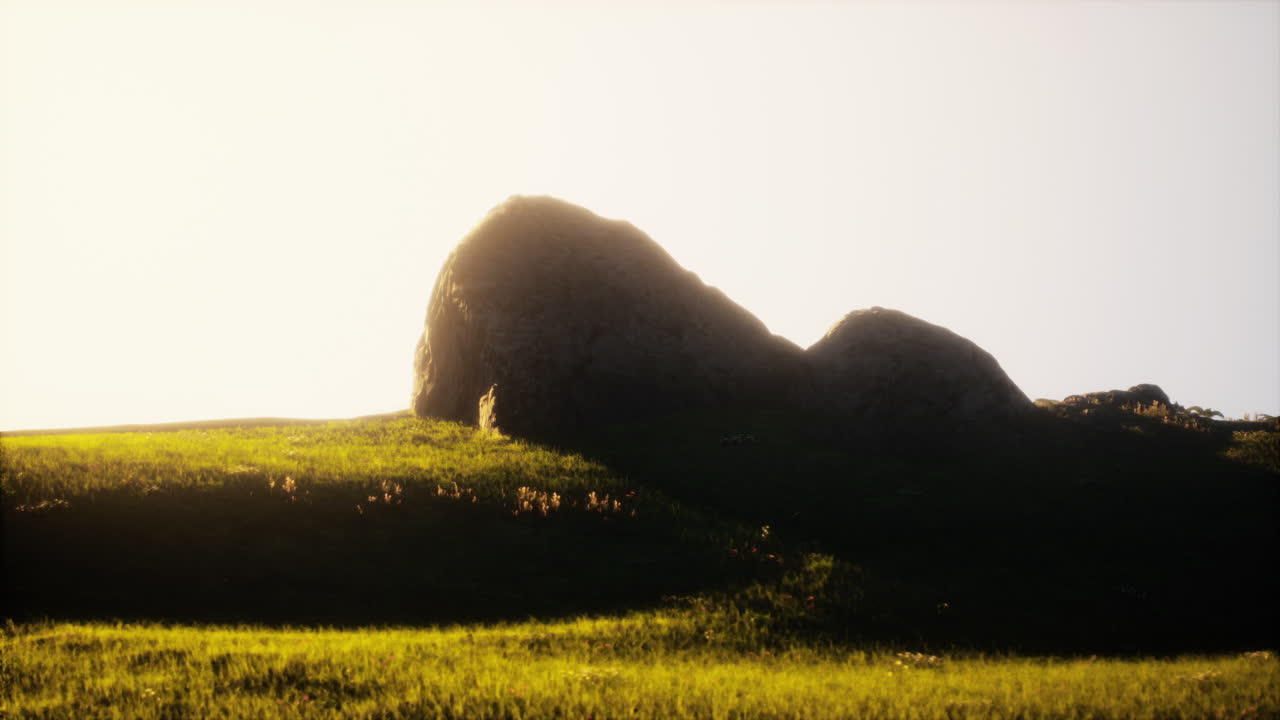 큰 바위와 함께 잔디 언덕 위에 해가 뜨는