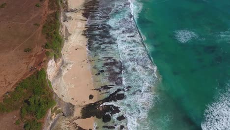 Vista-Alta-De-Los-Acantilados-De-Uluwatu-Y-La-Playa-Tomada-Desde-Un-Dron,-Hermosas-Olas-Rodando-Sobre-Una-Playa-Rocosa,-Filmada-En-Bali,-Indonesia