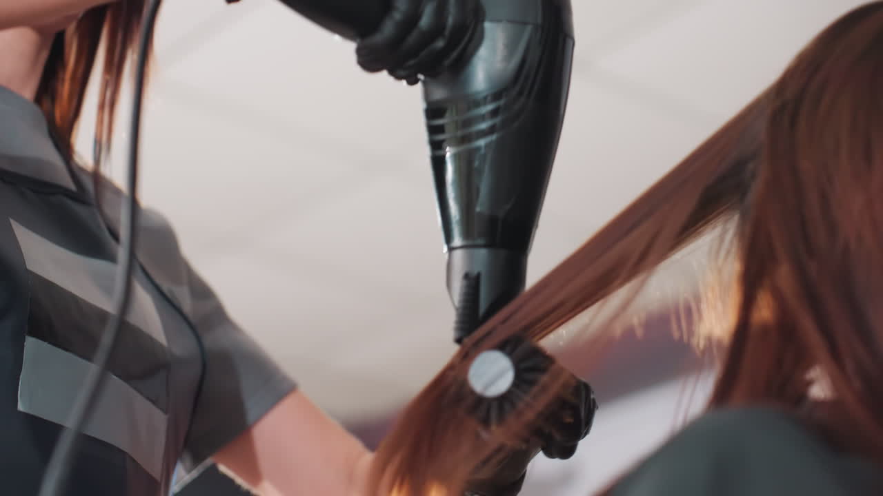 closeup caucasian stylist smoothing hair ends with brush and dryer, concentrated airflow shaping strands, glossy highlights catching light, careful gloves and rotation, salon detail shot