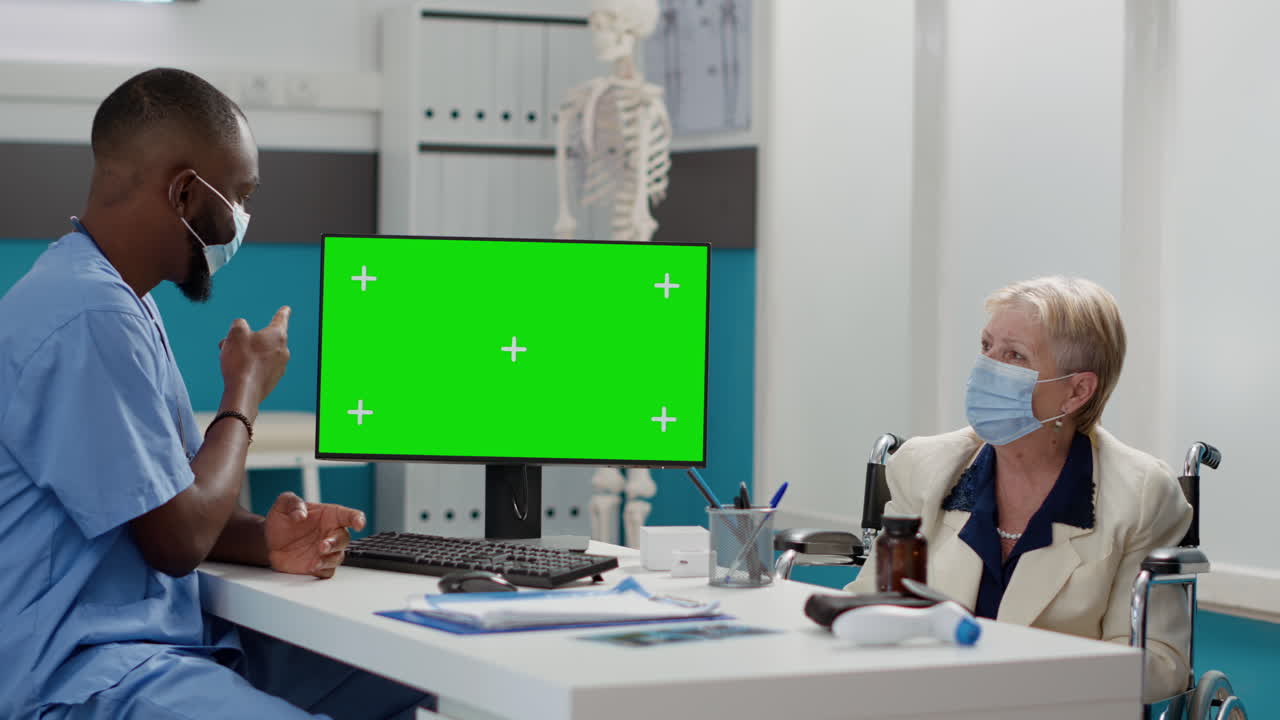 Doctor consulting with elderly patient with green screen monitor