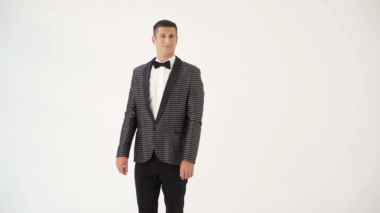a man in a checkered suit with a bow-tie is parodying manners of macho on a white background in the studio.