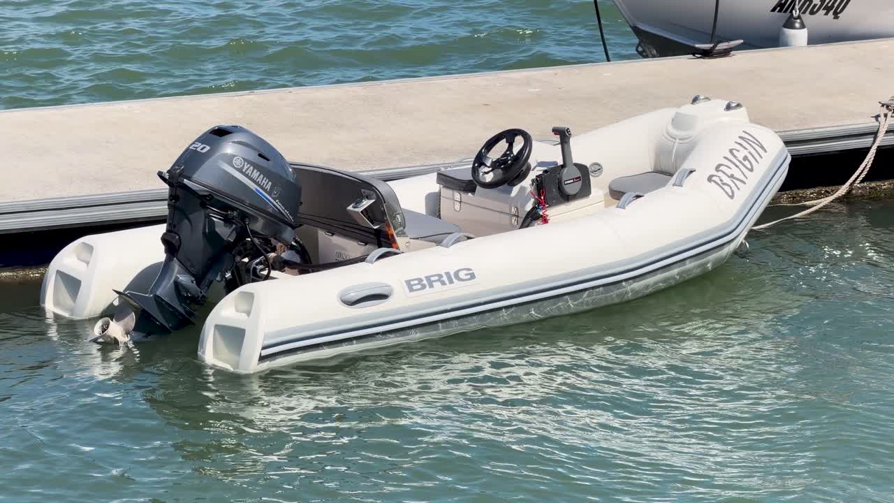 Un gommone gonfiabile bianco con un motore fuoribordo galleggia accanto a una banchina di cemento alla luce del sole