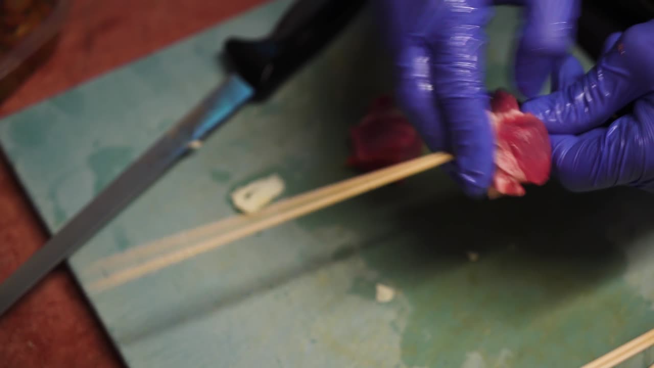 Hands of chef put meat of wooden skewer, close up