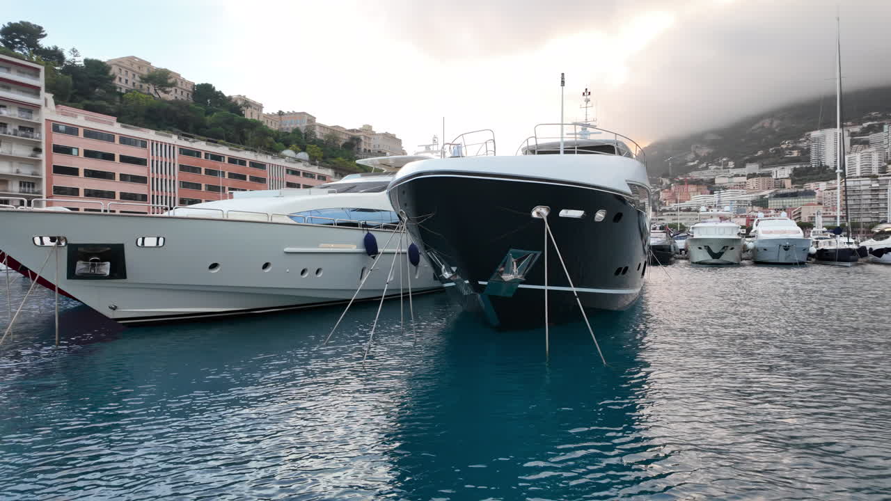 La Condamine, Monaco - 4 luglio 2025: fila di yacht di lusso ormeggiati a Port Hercules, con il paesaggio urbano di Monaco e le colline nebbiose sullo sfondo