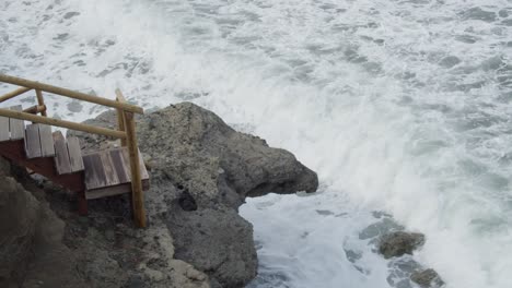 Cámara-Lenta,-Fuertes-Olas-Marinas-Salvajes-Chocando-Contra-Una-Escalera-De-Madera-Y-Rocas-En-Chipre