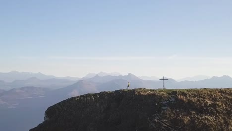 A-young-hiker-with-a-yellow-shirt-stands-next-to-a-summit-cross-and-looks-around