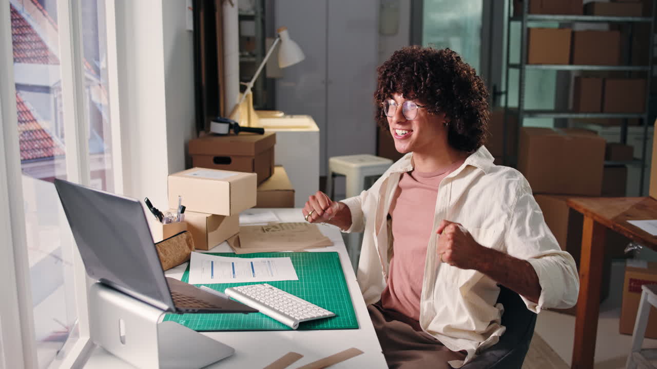 Giovane uomo che celebra il successo mentre lavora al laptop in ufficio.
