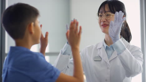 asian female doctor and boy high fiving in clinic