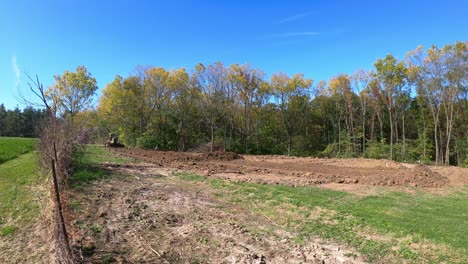 Wide angle view of a yellow bulldozer leveling soil at a construction site with wooded area in background in early autumn
