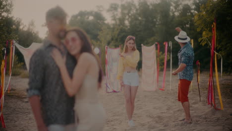 young couple dancing near friends embracing at beach