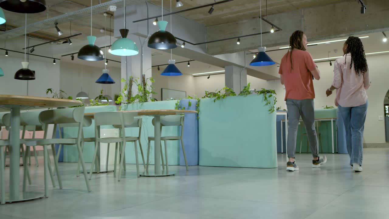 Dos compañeros de trabajo afroamericanos caminando por un salón de planta abierta después de una breve charla, compartiendo un teléfono