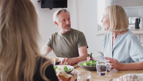 family with senior parents and adult offspring eating meal around table at home together