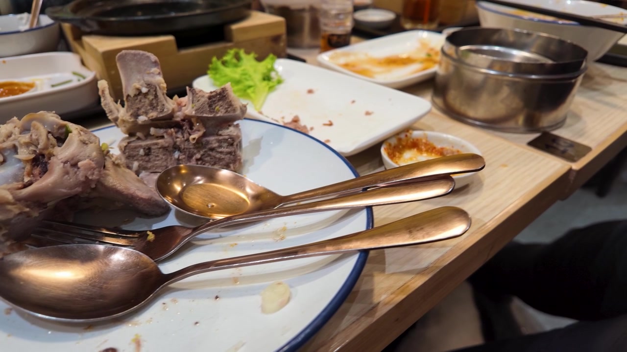 Close-up of finished beef rib bones on a dirty plate with silverware in Bangkok, Thailand.