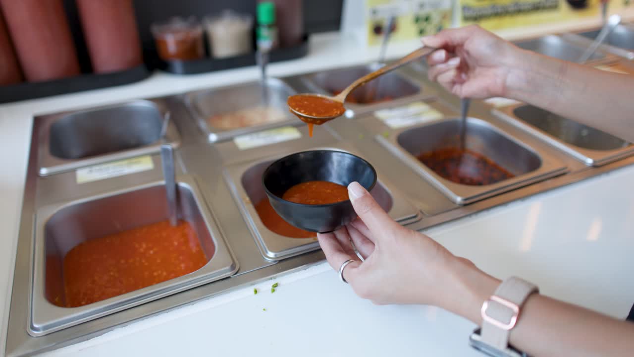 Primo piano di mani che prelevano salsa chili rossa in una ciotola a un buffet.