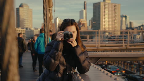 woman taking photo on brooklyn bridge at sunset