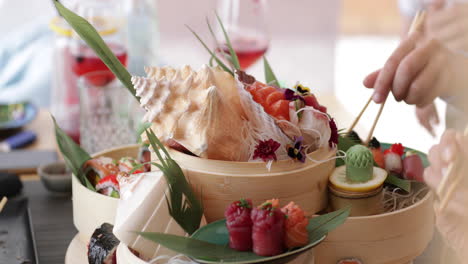 person picking fresh sushi on a platter decorated in seashells, flowers, and green leaves