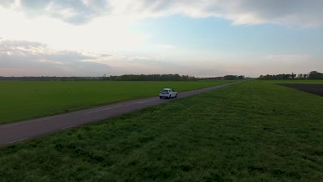 Luftdrohnenaufnahme-Eines-Weißen-Autos,-Das-Abends-Auf-Einer-Schmalen-Landstraße-In-Südschweden-Skåne-Fährt